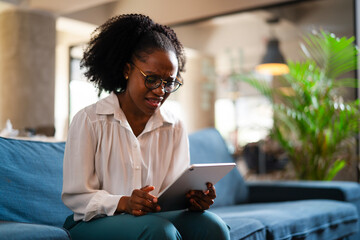 Beautiful African businesswoman sitting on sofa in office. Young woman using digital tablet.