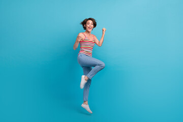Full body photo of delighted cheerful lady jumping raise fists triumph luck isolated on blue color...