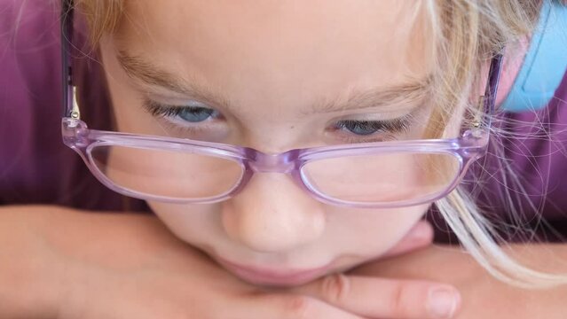A little blonde girl watches cartoons on a phone or tablet. Close-up view of kid girl face watching video on phone or tablet.