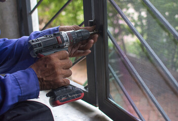 man using electric screwdriver on window steel frame