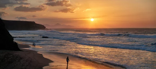 Badezimmer Foto Rückwand Fuerteventura, Strand von La Pared - malerischer orangefarbener Sonnenuntergang, eine junge Frau und ein fotografierendes älteres Paar stehen barfuß im nassen Sand © Robert Schneider
