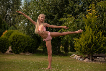 A little girl is professionally engaged in gymnastics and shows her skills in the summer on the street - Powered by Adobe