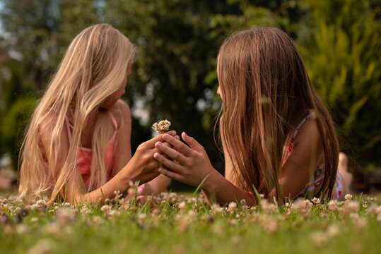 Two girls lie and talk on the green grass at the dacha in summer in swimsuits and have fun