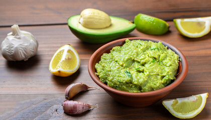 Clay bowl with fresh guacamole, lemon and garlic on wooden table. Diet vegetarian Mexican food avocado.
