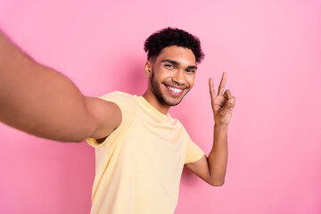 Portrait of optimistic pleasant man afro hair earrings stubble recording video for blog showing v-sign isolated on pink color background