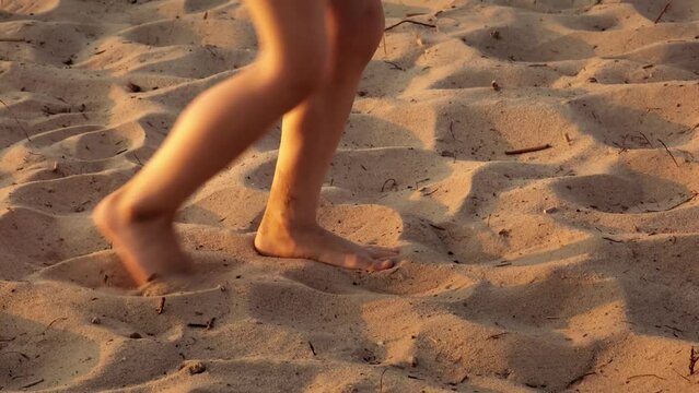 Legs of walking child on dry sand beach close-up. Moving barefoot in sunset lights. Summertime sandy background. Travelling. Vacation concept. Sea holiday. Happy childhood. Healthy lifestyle.