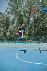 Slam dunk. Full-length image of young man in motion, playing basketball outdoors on sportsground on...