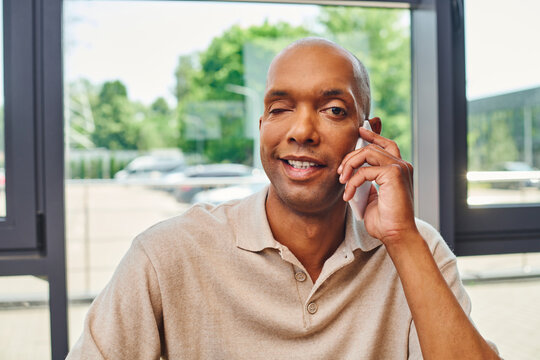 myasthenia disease, happy african american man at work, cheerful and dark skinned office worker with ptosis syndrome talking on smartphone, inclusion, corporate culture