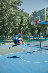 Slam dunk. Full-length image of young man in motion, playing basketball outdoors on sportsground on...