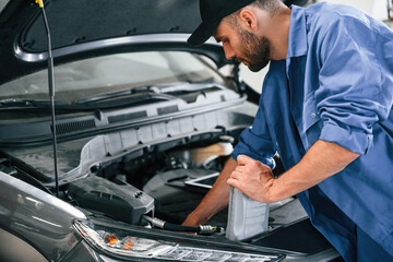 Fototapeta na wymiar Grey colored oil can in hands. Auto mechanic working in garage. Repair service