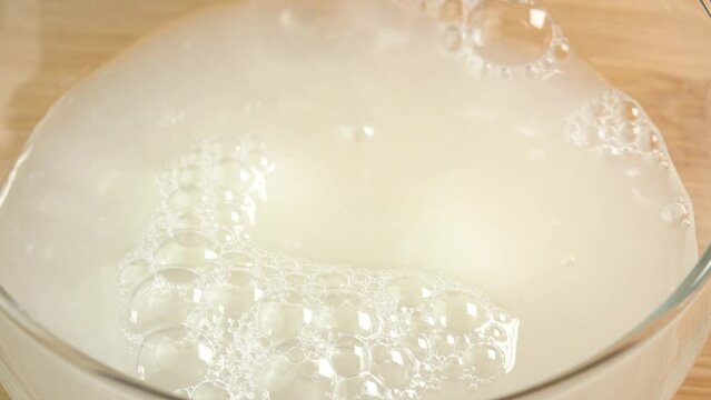 Mozzarella cheese balls are poured along with whey into a glass bowl. Ingredients for making pizza or fresh tomato salad