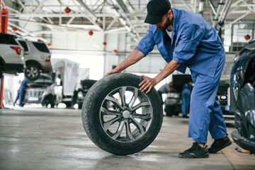 Obraz na płótnie Canvas New tire, moving it. Auto mechanic working in garage. Repair service