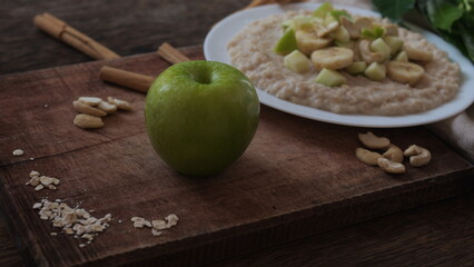 Plate of oatmeal porridge with green apple, cashew and banana. Close up.