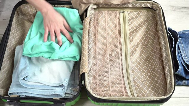 Man packing his suitcase for long journey with wad of money. Guy closes the green baggage case with clothes in hand luggage zip up zipper. Tourist packing things for a trip. Long awaited vacation