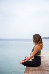 Fototapeta na wymiar Woman practicing yoga by the sea on a deck - Padmasana / Lotus pose / meditation sitting - chin mudra