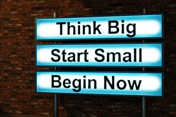 Obraz premium Think Big, start small, begin now. Black letters on a blue illumintaed light box, red brick wall. Thinking, ideas, beinnings. small business, strategy, motivation, encouragement. 3D illustration