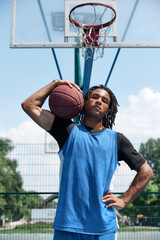 Portrait of young man with wearing blue uniform, posing with basketball ball on outdoor...