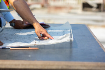 close up hand architect Engineering man in safety hardhat looking at blueprint at factory industrial facilities. Heavy Industry Manufacturing Factory. Prefabricated concrete walls. Asian worker team