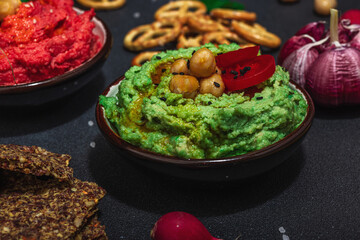 Various hummus dips, fresh vegetables and herbs. Crispy bread snacks, modern vegan healthy food