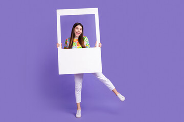 Full length photo of crazy playful girl dressed flower print t-shirt holding photo frame having fun isolated on violet color background © deagreez