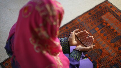 Closeup of a muslim woman hands while praying with prayer beads on prayer rug.
