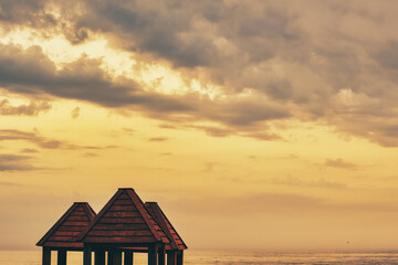 Roofs of wooden arbors against the sunset sky over the ocean, sea, or lake.