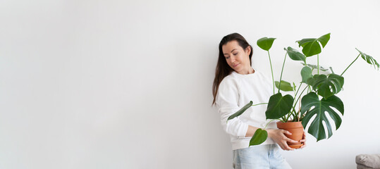 Young millennial woman holding a pot with green monstera house plant. Horizontal banner.