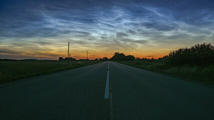 Noctilucent (silverly) clouds over straight road after sunset.
