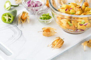 A cutting board topped with a golden berry salsa and surrounded by ingredients.