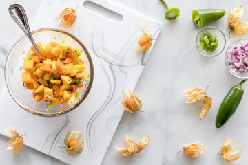 A bowl of homemade golden berry and mango salsa surrounded by ingredients.