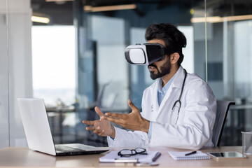 Portrait of a young Indian doctor sitting at a table in a hospital, wearing a virtual mask