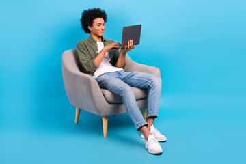 Portrait of positive handsome man perming coiffure khaki shirt sit in armchair look at new laptop...