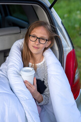 A child wrapped in a white blanket is sitting in the trunk of a car