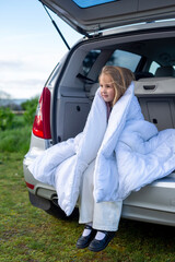 A child wrapped in a white blanket is sitting in the trunk of a car