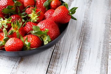 Fresh organic strawberries in a black round plate on a light wooden background.