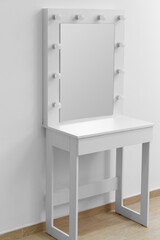 Modern white makeup dressing table with mirror and backlight against a white wall.