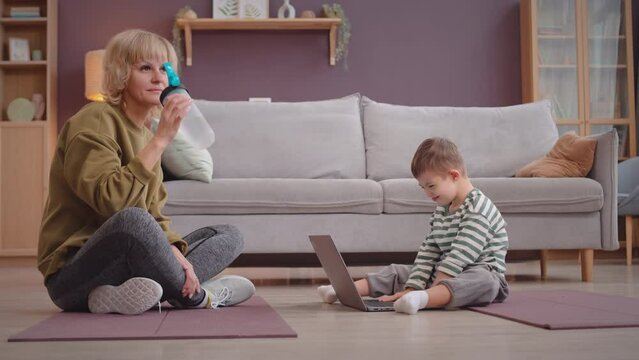 Caucasian mother giving water to her 6 year old son after having domestic physical therapy on mat in living room