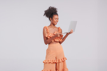 A digital fashion maven, a black girl in an orange shirt poses in a studio fashion shoot with a laptop, embracing the fusion of style and technology.