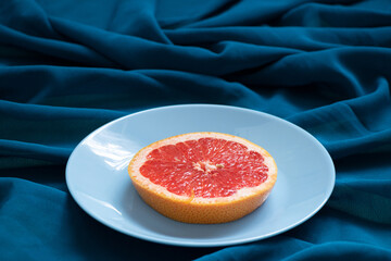 A slice of grapefruit lies on a plate on a wavy blue tablecloth as a background, vegan food