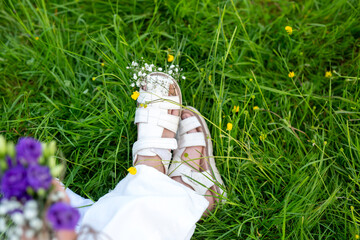Children's feet in sandals in the grass with flowers