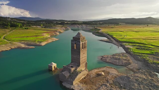 Clock tower of the Iglesia del Mediano, submerged in a Pyrenean swamp at sunset during storm. Dron shot descending.