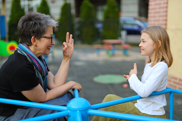 Happy mom and daughter communicate with sign language on the playground.