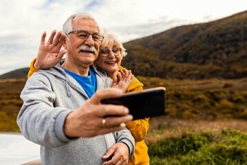 Senior couple esting after hiking in countryside making selfie with smartphone.