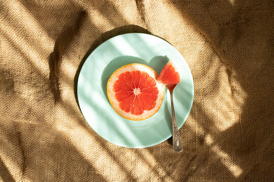 A Slice Of Grapefruit Lies On A Plate With A Spoon On A Wavy Brown Burlap As A Background, Vegan Food