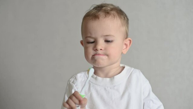 the kid is brushing his teeth with a toothbrush on a gray background. Oral hygiene. 