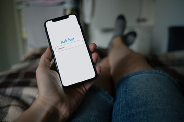 Person laying down on couch and asking questions from chat bot on smartphone