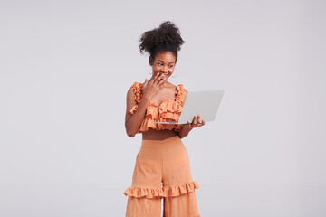 Exuding studio tech chic, a black girl in an orange shirt holds a laptop, adding a modern touch to her fashion shoot in the studio.