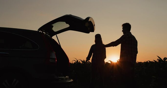 A young couple is arguing in front of a broken car. The car is parked on the side of the corn field