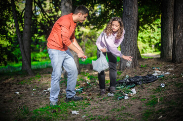 Young couple collect garbage thrown in nature park. Protection, maintenance and preserve of the eco...