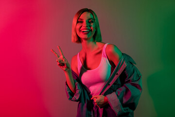 Photo of good mood lady youth greetings with v sign gesture in cyber discotheque isolated on gradient neon color background